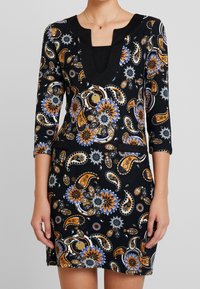 Robe noire à motifs paisley avec des manches trois-quarts, décolleté en cœur, ornée de motifs floraux orange, bleu et blanc ; comprend deux poches latérales.