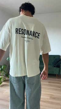 Λευκό oversized t-shirt με μαύρο κείμενο "RESONANCE" και "Creative Collection" στην πλάτη. Συνδυάζεται με ανοιχτό μπλε φαρδύ τζιν.