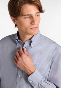 Camicia azzurro chiaro con bottoni realizzata in tessuto testurizzato, con un piccolo logo di un cavallo ricamato sul petto e polsini standard.