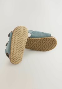 Sandali blu scamosciati con cinturini regolabili, suole in gomma beige testurizzate con un motivo a zigzag e una finitura liscia sulla parte superiore.