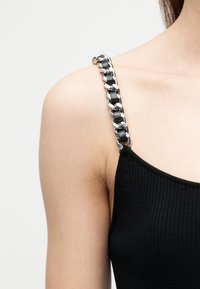 Ώμος και άνω βραχίονας ενός ατόμου που φοράει μαύρο ριμπ top με ασημένια αλυσίδα και μαύρο δερμάτινο λουράκι ως λεπτομέρεια στον ώμο.