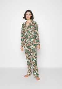 Blumiges Pyjama-Set in Grün, mit weißen, rosa und orangen Blattmustern. Langärmlige Bluse mit Kragen und lange Hosen. Baumwollstoff.