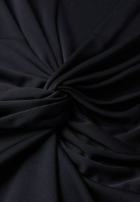 Tissu noir torsadé au centre, montrant des plis doux et une texture lisse en gros plan.