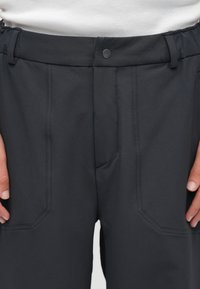 Melnas bikses no viegla auduma. Ir brīva piegriezuma, ar elastīgu jostasvietu un pogas aizdari, kā arī slīpiem priekšējiem kabatām.