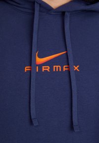 Jūros mėlynos spalvos džemperis su virvelėmis, su oranžine Nike swoosh logotipo ir "AIRMAX" tekstu ryškiai oranžine spalva. Lygaus paviršiaus audinys.