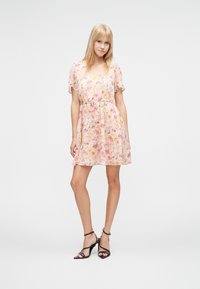 Φλοράλ φόρεμα σε ανοιχτό ροζ, με κοντά μανίκια με βολάν, ντεκολτέ σε σχήμα V και ζώνη με κορδόνι στη μέση. Διαφανές, ελαφρύ ύφασμα με λεπτό σχέδιο.