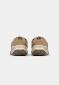Pantofi sport maro cu o talpă din cauciuc texturat, superior din țesătură elastică și bandă de tragere la spate. Design minimalist cu talpă de culoare crem în contrast.