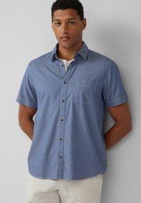 Koszula z krótkim rękawem, jasnoniebieska, zapinana na guziki, wykonana z tkaniny chambray. Posiada kieszeń na piersiach i brązowe guziki. Gładka faktura i luźny krój.