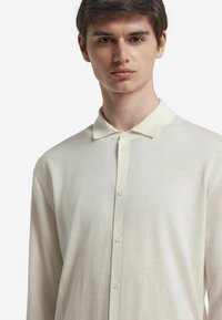 Ljusbeige långärmad polo tröja i mjukt och slätt tyg, med krage och fem knappar framtill.