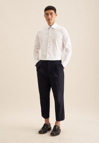 Witte overhemdbloes met een kraag, gecombineerd met marineblauwe cropped broeken en zwarte leren schoenen. Minimalistisch ontwerp, zonder patronen of accenten.