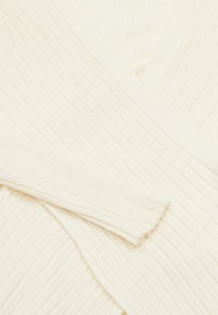 Maglione a coste color crema con scollatura a V, caratterizzato da un tessuto testurizzato e un aspetto morbido e leggero.