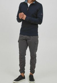 Marinefarbener Zip-Hoodie mit kontrastierendem Kragen, kombiniert mit grauen Cargo-Hosen mit elastischen Bündchen und seitlichen Taschen sowie schwarzen Sneakers.