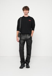 Melnas garām piedurknēm krekls ar sarkanu logo, kopā ar melnām ādas kravas biksēm ar lielām kabatām un šauru piegriezumu. Melnas sporta apavi.