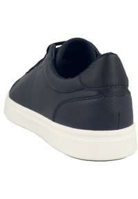 Zapatilla de deporte de cuero azul oscuro con suela de goma blanca. Punta redonda, textura suave, cuello acolchado y diseño minimalista con costuras a tono.