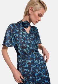 Sukienka z krótkim rękawem z przezroczystego materiału w niebiesko-brązowy wzór w panterkę. Zawiera dopasowany szalik związany na dekolcie.