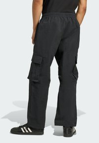 Čierne cargo nohavice s textúrovaným povrchom, so voľným strihom, elastickým pásom a viacerými bočnými vreckami. Nosené s čiernymi teniskami.