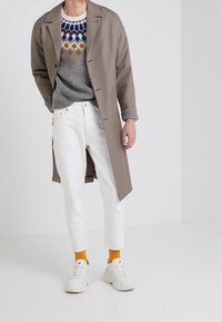 Beige rutigt jacka, grå stickad tröja med färggat mönster, vita jeans och klumpiga vita sneakers med orangea strumpor.