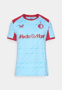Gaiši zils sporta krekls ar sarkaniem plecu un piedurkņu akcentiem, Feyenoord Rotterdam logo, Castore logo un MediaMarkt sponsora teksts priekšpusē.