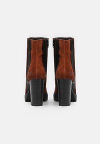 Bottines en daim noir et marron avec un talon haut épais, fermetures éclair latérales et un logo discret sur le talon. Surfaces lisses et texturées.