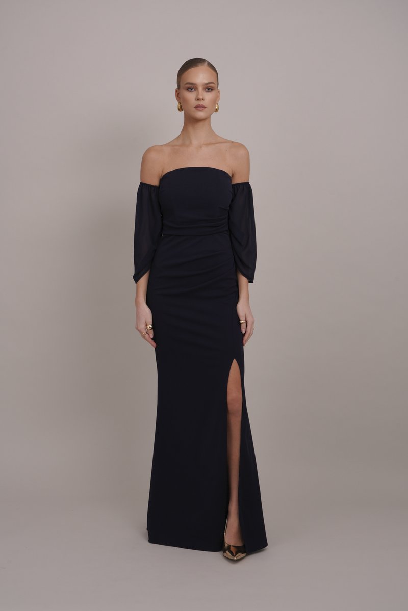 Robe bleu marine à épaules dénudées avec de longues manches amples, fente haute sur la cuisse et silhouette ajustée, fabriquée en tissu lisse et extensible.