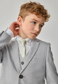 Giacca di abito grigia chiara con tessuto texturizzato, design a un bottone, due bottoni, camicia bianca e cravatta verde con motivo.