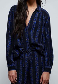 Schwarze Button-Down-Bluse mit blauem Blumenmuster und vertikalen Streifen, mit langen Ärmeln, einem Bindegürtel in der Taille und einem lockeren Schnitt.