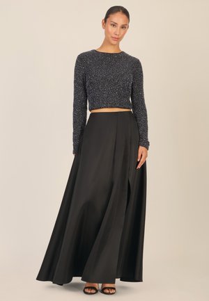 Zwarte high-waisted rok met plooien, gecombineerd met een cropped marineblauw top met een gestructureerd ontwerp en lange mouwen. Sandalen maken de look compleet.