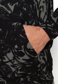 Czarny i szary sweatshirt z wirującymi, abstrakcyjnymi wzorami, z boczną kieszenią i prążkowanym dołem. Widoczna jest miękka tekstura materiału.