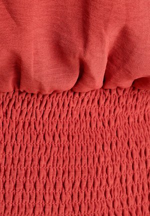 Textil rojo que presenta una sección superior lisa y sin textura y una sección inferior fruncida y texturizada con un patrón arrugado.