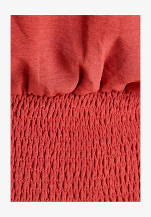 Textil rojo que presenta una sección superior lisa y sin textura y una sección inferior fruncida y texturizada con un patrón arrugado.