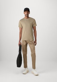 Khaki kortærmet t-shirt, beige bukser, sort kasket og en sort tekstureret totebag; hvide sneakers fuldender outfittet.