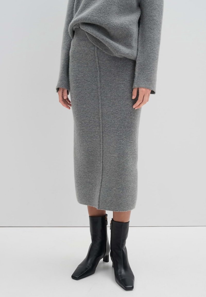Personne portant une jupe midi en maille grise et un pull assorti, accompagnés de bottines en cuir noir à talons blocs et fermetures éclair latérales.