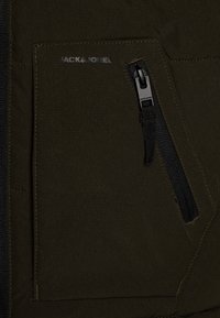 Giacca imbottita verde scuro con tasca con zip, tessuto resistente e dettagli cuciti. Logo "JACK & JONES" stampato sulla tasca.