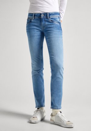 Světle modré džíny z denimu se slim fit, klasickým designem s pěti kapsami a jemnými detaily prošívání, v kombinaci s bílými teniskami.