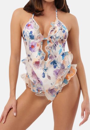 Costume intero floreale con bordi arricciati, scollo a V profondo e spalline halter su una donna su sfondo semplice.