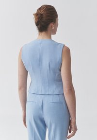 Světle modrý dokonalý bezrukávový top se strukturovaným designem, jemnou texturou a zkráceným lemem, spárovaný s odpovídajícími elegantními kalhotami.