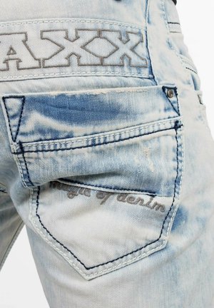 Lichtblauwe denim jeans met een versleten textuur, voorzien van een achterzak met geborduurde tekst "Magic of denim" en een logo patch.