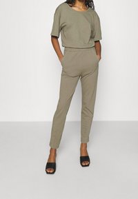 Top de punto verde oliva con mangas cortas, combinado con pantalones ajustados a juego. Las sandalias negras de tiras completan el conjunto.