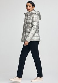 Silverfärgad puffjacka med luva, har quiltad design och sidofickor. Bärs med svarta byxor och ljusa sneakers för en avslappnad look.