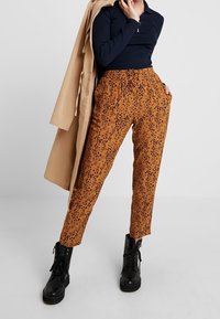 Hnědé kalhoty s černým tečkovaným vzorem, elastický pas, zúžené nohavice, ve spojení s námořnickým topem a černými armádními botami.