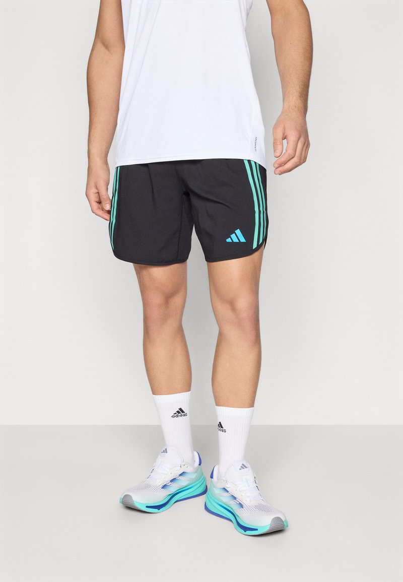 Fekete sportnadrág, világoskék oldalsávokkal, adidas logóval. Fehér zoknikkal és könnyű, sokszínű futócipőkkel párosítva.