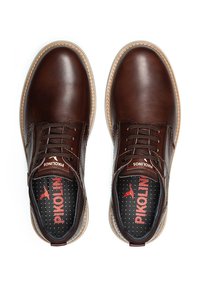 Zapatos de cuero marrón con un acabado suave, puntera redonda y diseño de cordones. Suela de un marrón claro contrastante y plantilla acolchada con patrón de puntos.