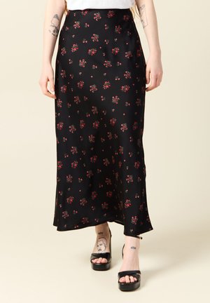 Schwarze Satin-Maxi-Rock mit kleinem roten Blumenmuster. Enganliegende Passform, glatte Textur und leichter Glanz. Getragen mit schwarzen Plateau-Sandalen.