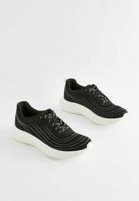 Black athletic shoes with a textured knit upper, white cushioned sole, and striped detailing. Features black and silver laces.