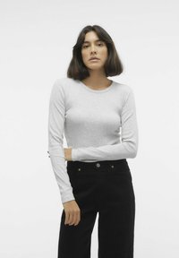Maglietta a maniche lunghe grigio chiaro con scollo rotondo, texture liscia e stile aderente abbinata a jeans neri a vita alta con accessori dorati.