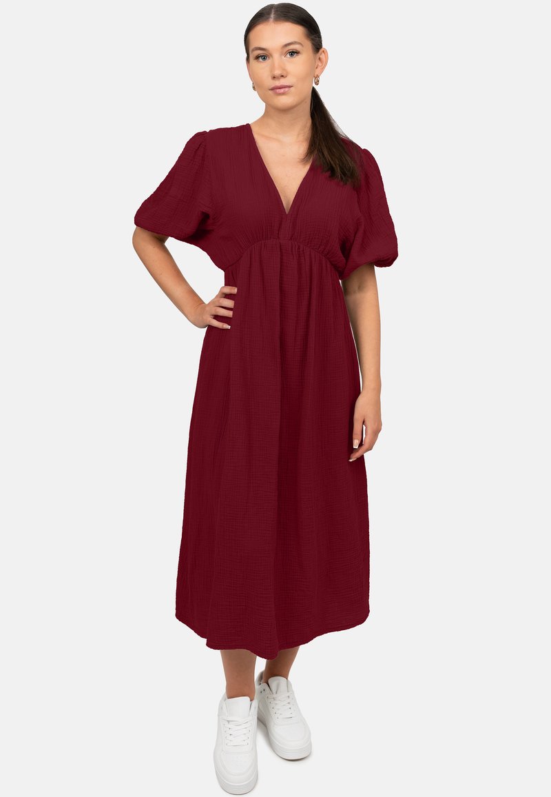 Bordeaux midi-jurk van textuurstof, met een V-hals en pofmouwen, gecombineerd met witte sneakers voor een casual look.