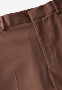 Pantaloni marroni con una texture liscia e tessuta, dotati di una vita aderente e di una cucitura intricata lungo le cuciture e le tasche.