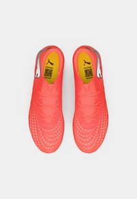 Zapatillas de fútbol de color rosa brillante con una superficie texturizada, que cuentan con una plantilla amarilla y detalles grises. Los cordones son sencillos para un aspecto estilizado.