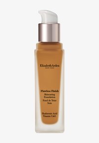 Fond de teint soin "Flawless Finish" dans une bouteille en verre transparent avec une section en ambre mat. Présente une pompe blanche et une étiquette avec du texte noir.