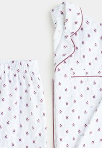 Ensemble de pyjama blanc avec haut à manches longues et pantalon à taille élastique, orné d’un petit motif de gouttes rouges et bleues et d’un passepoil bordeaux sur le col et la poche.